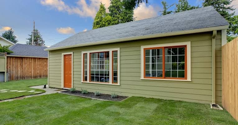 Single-story ADU with grey siding, a gabled roof, and a covered front porch, set on a lawn